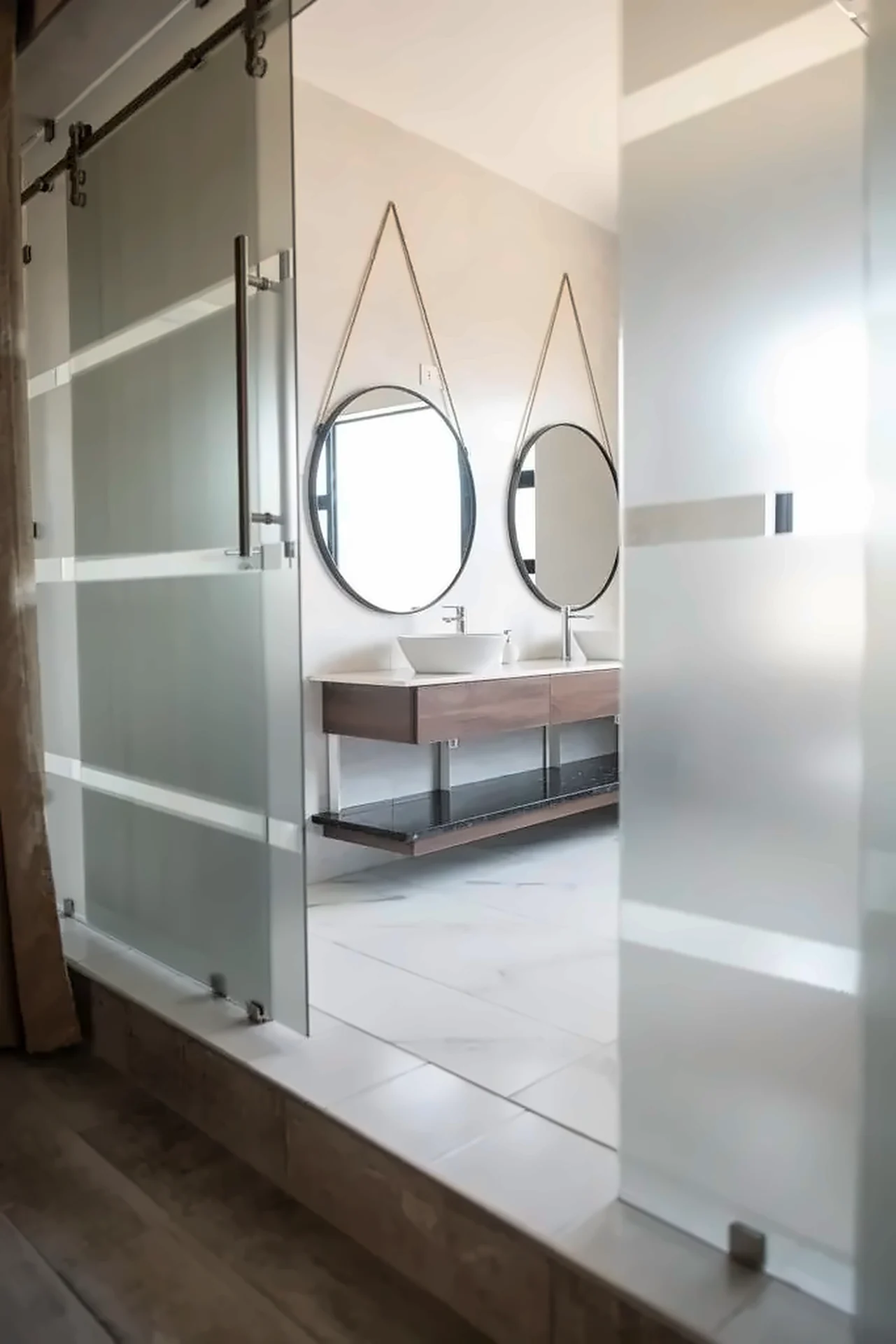 Frosted glass sliding door opening to a timber vanity with twin mirrors