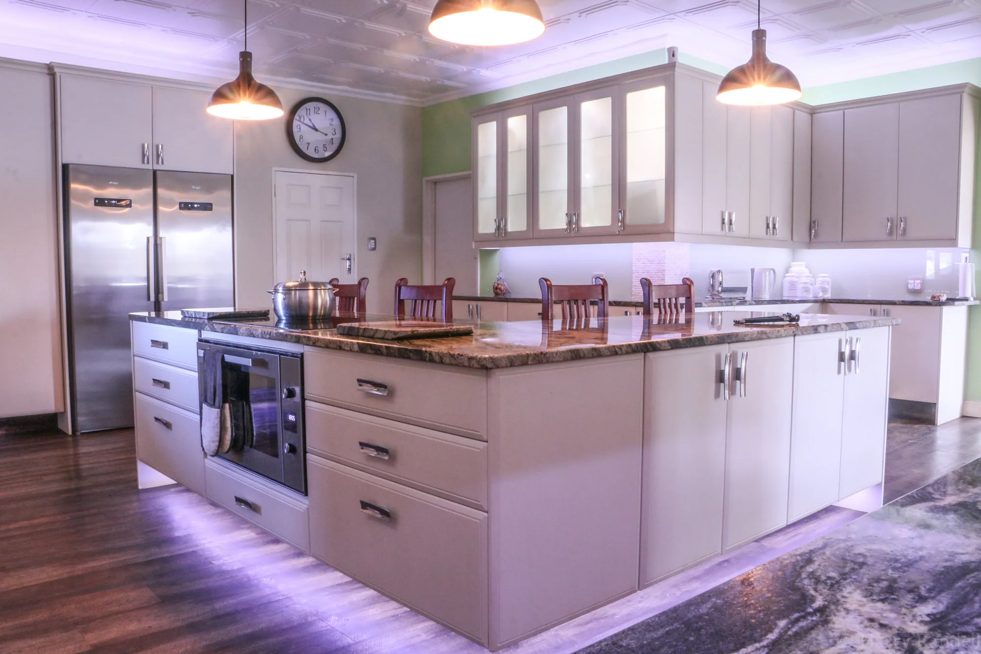Kitchen island with plinth lighting, glazed wall cabinets and pendant lamps