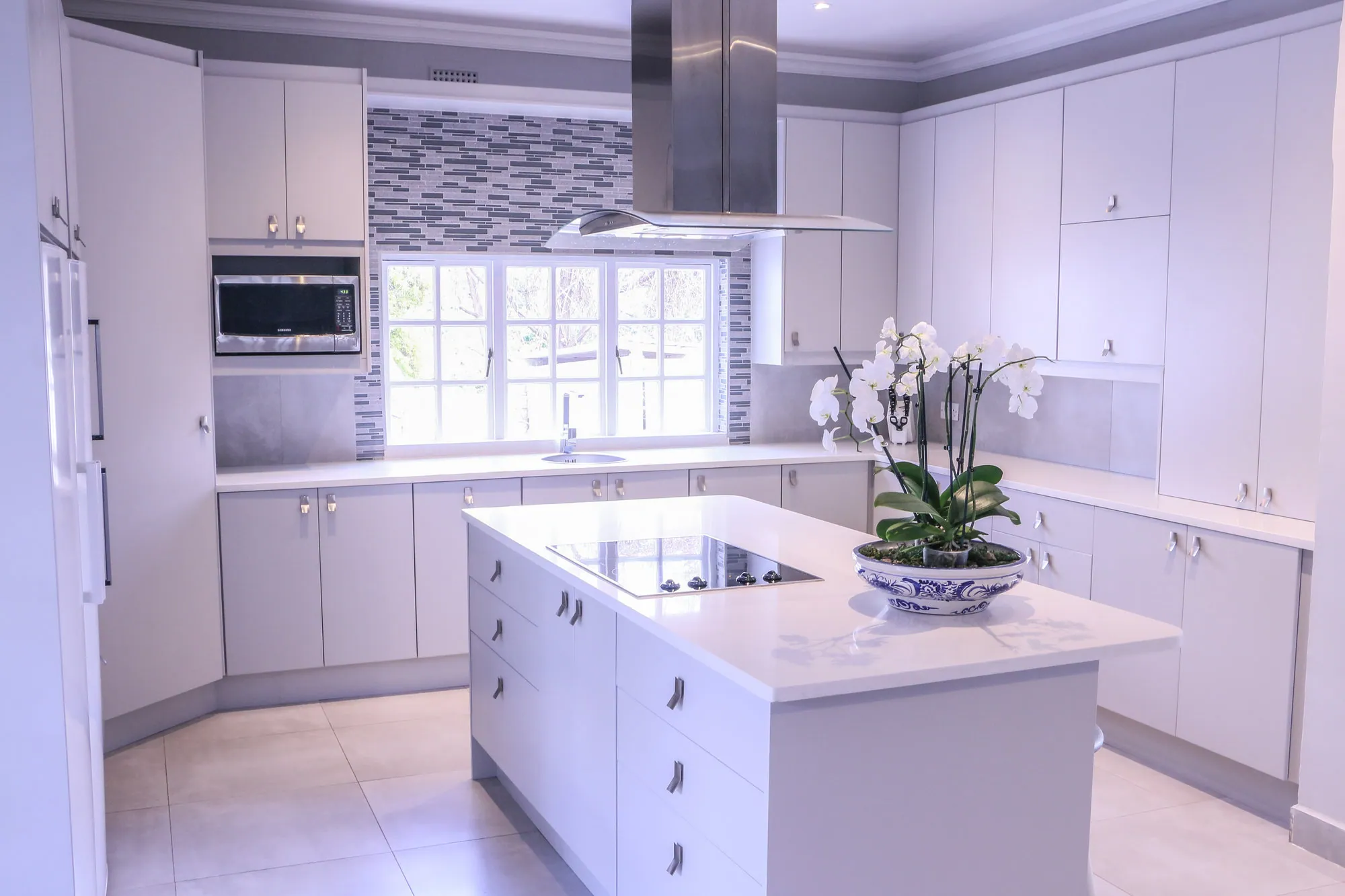 White kitchen with an island, stainless canopy and mosaic tiled splashback