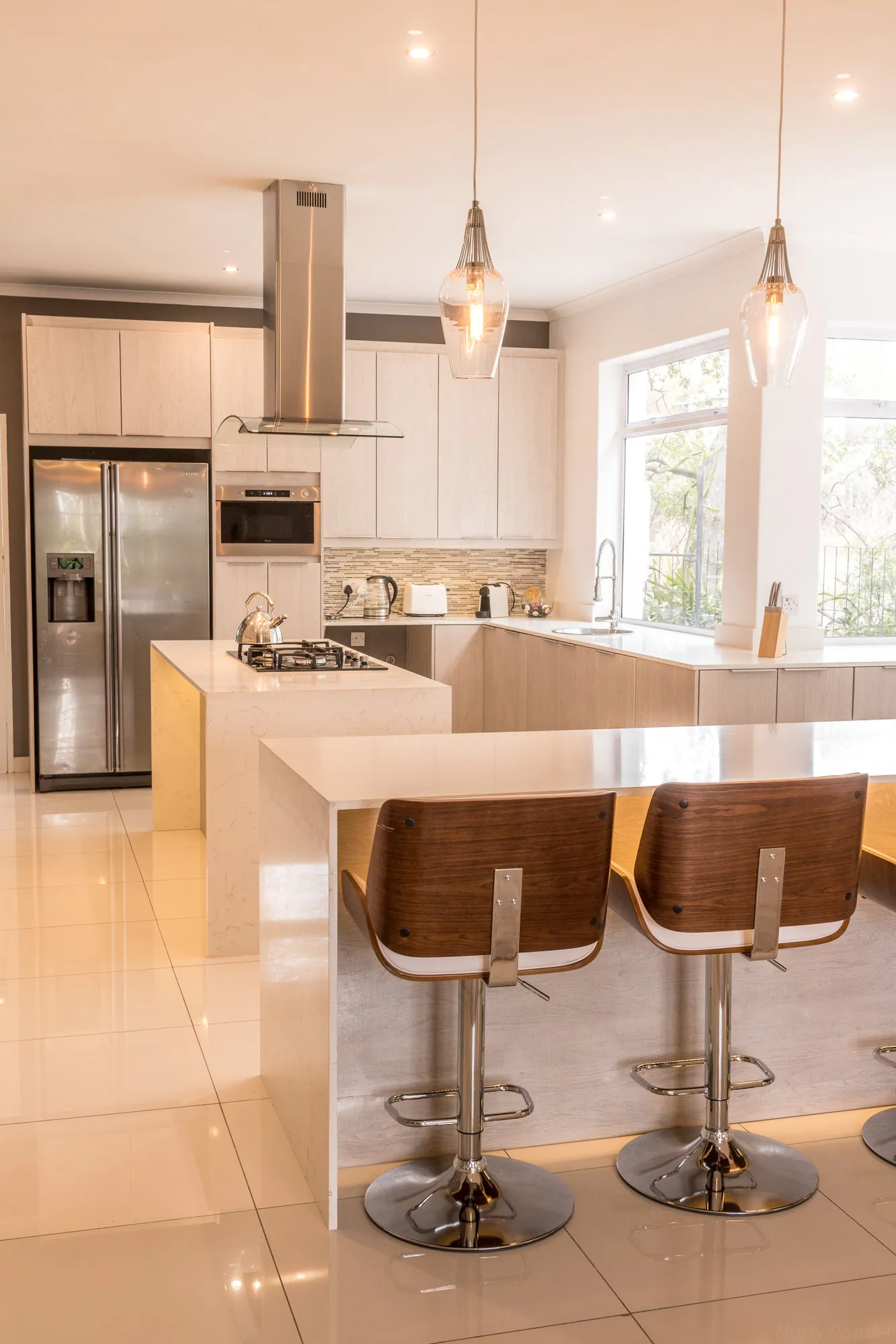 Kitchen island with timber and chrome bar stools beneath glass pendants