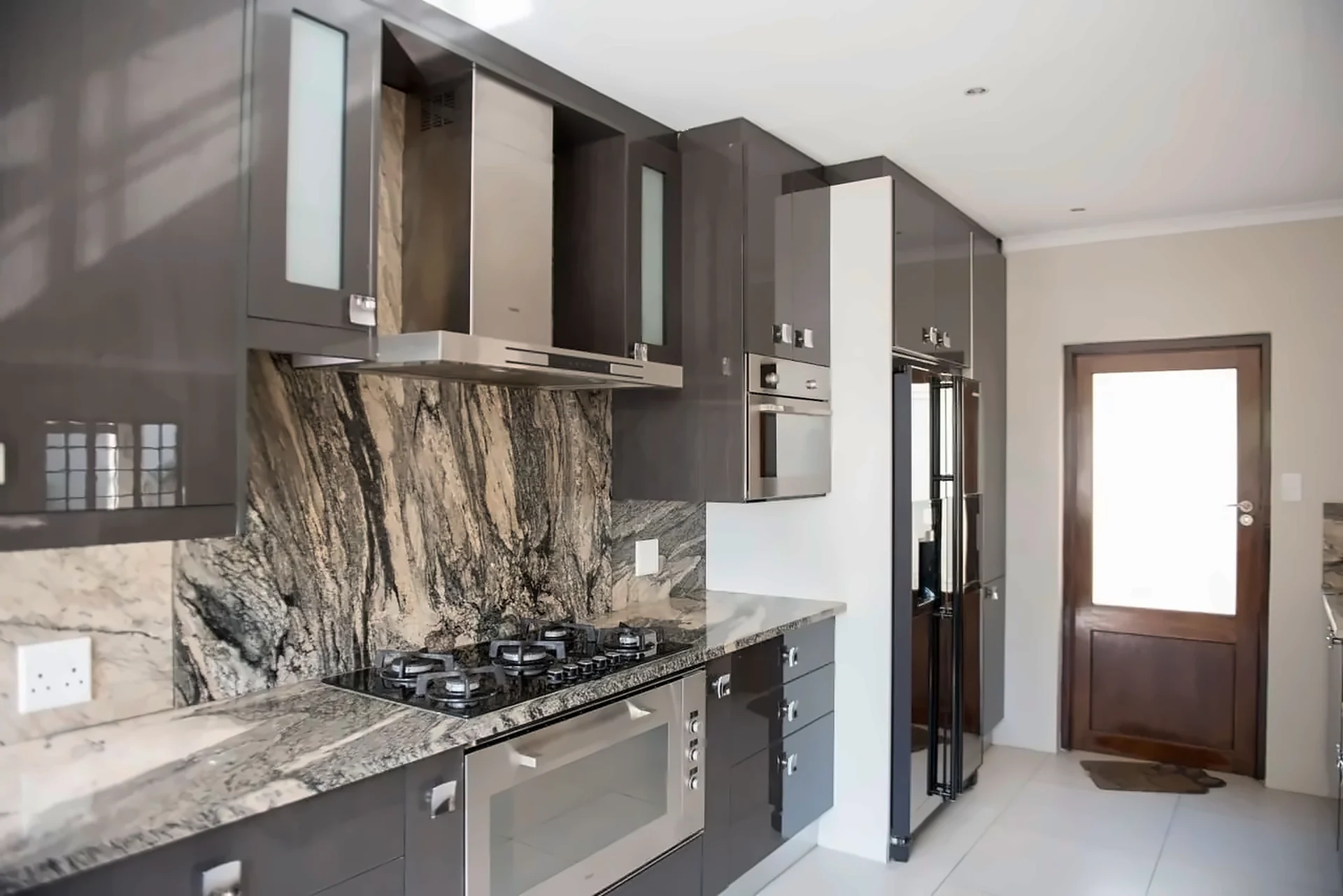 Dark kitchen with marble splashback, stainless extractor and tall oven units