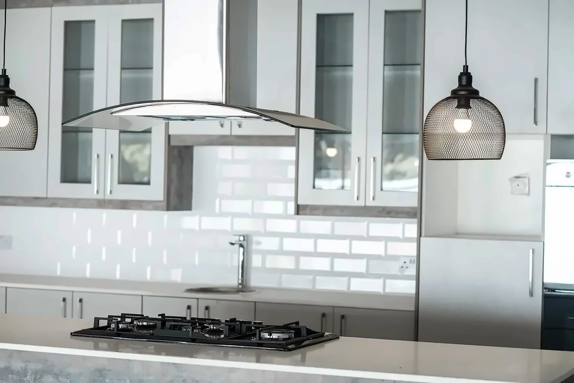 Glazed wall cabinets and white bevelled tiles behind an island gas hob