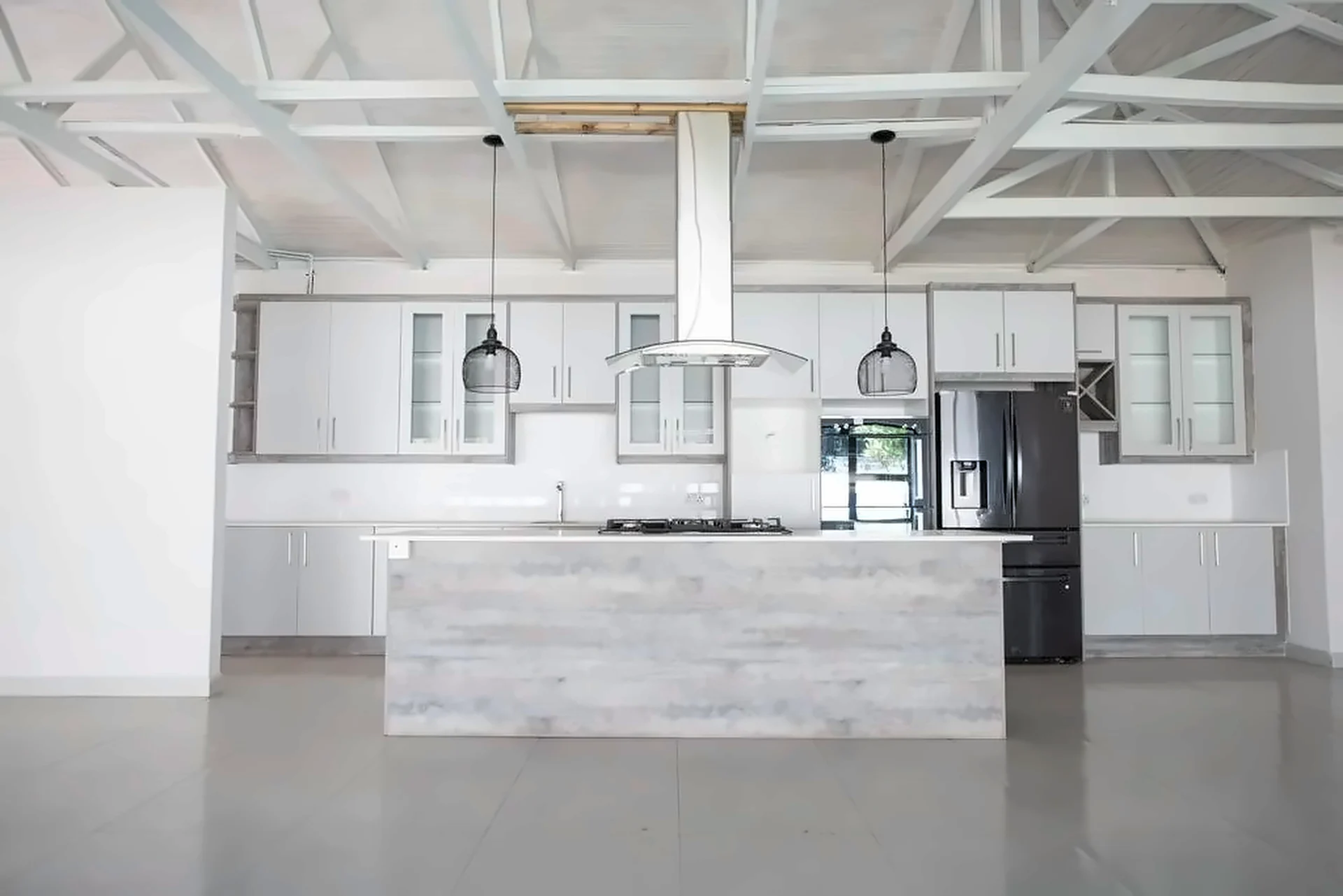 Long grey kitchen island with gas hob under exposed white roof trusses