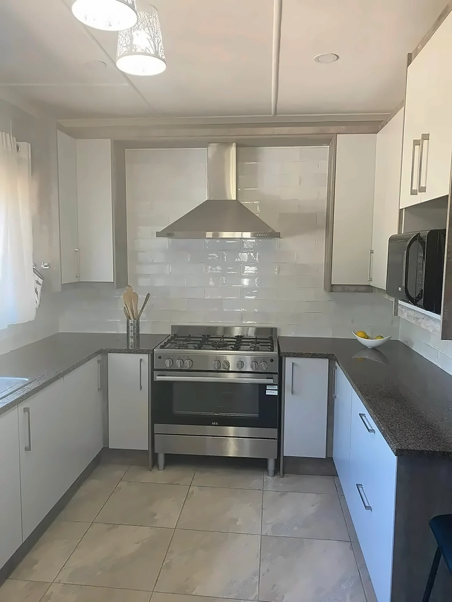 White kitchen with grey worktops, tiled splashback, range cooker and tall fridge housing