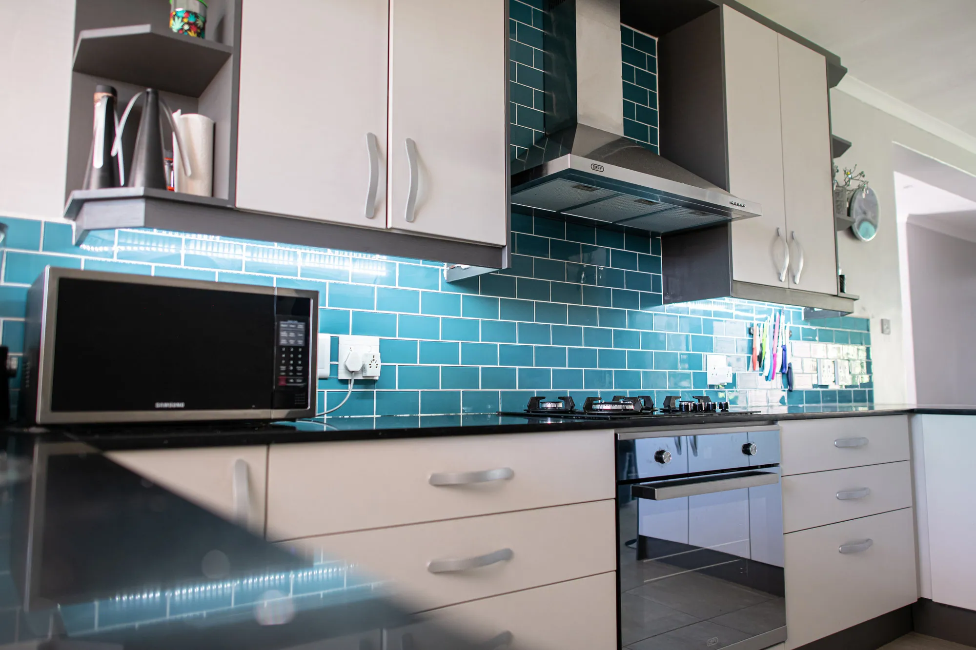 Teal subway-tiled wall with white cabinets, chimney extractor and under-cabinet lighting