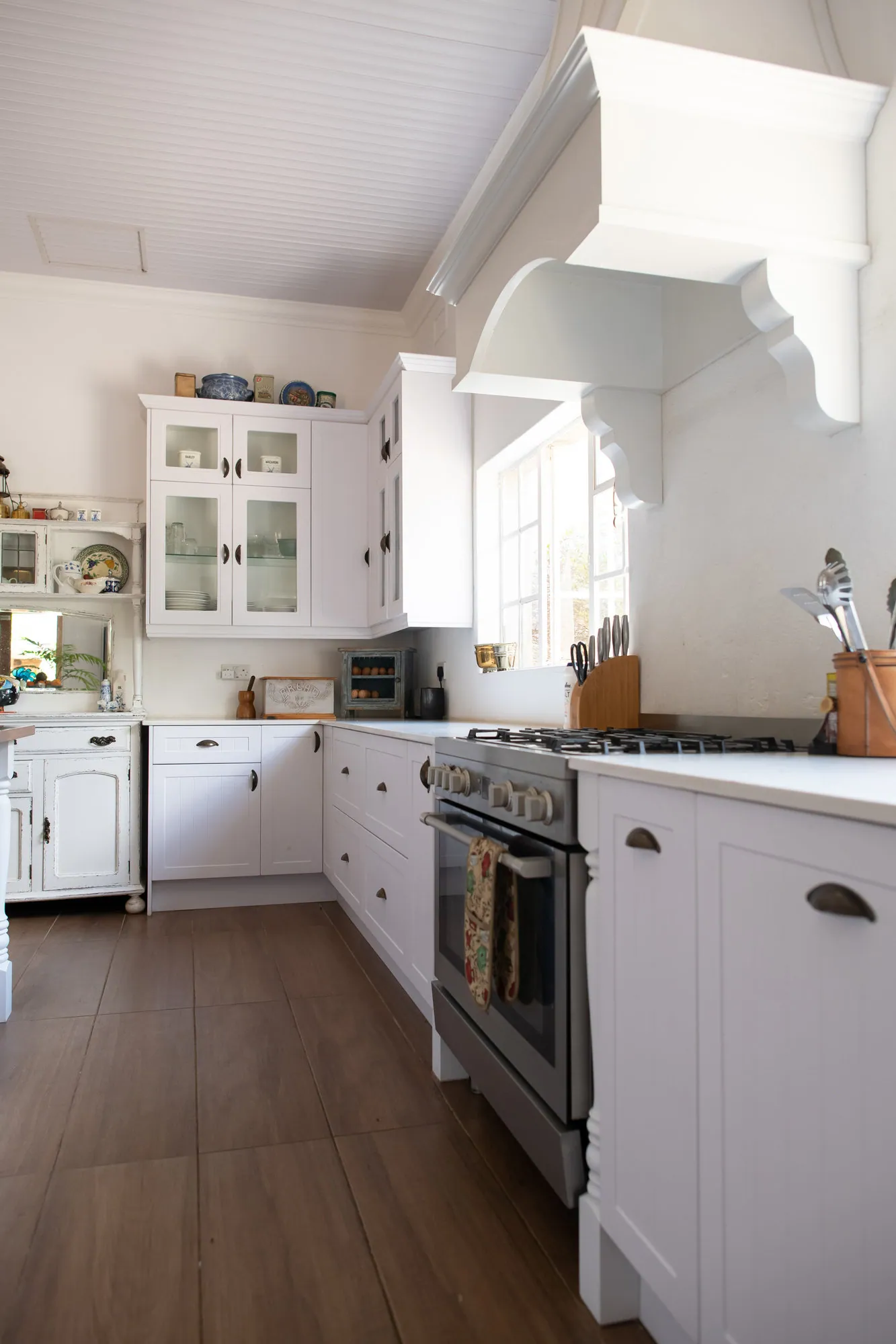 White painted kitchen with corbelled canopy, glazed dresser units and stainless oven
