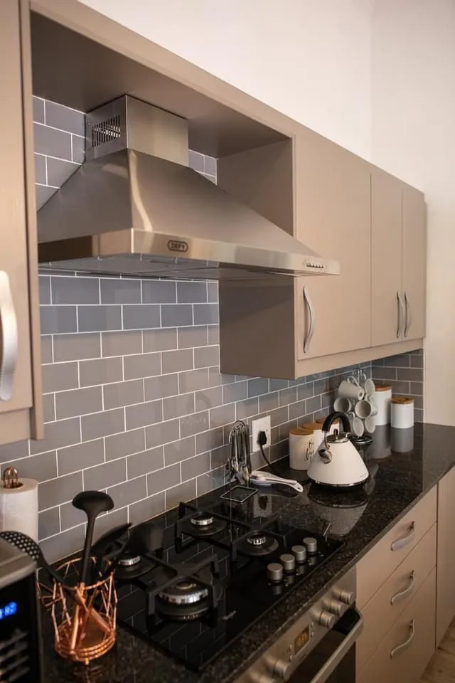 Gas hob on black granite with blue-grey subway tiled splashback