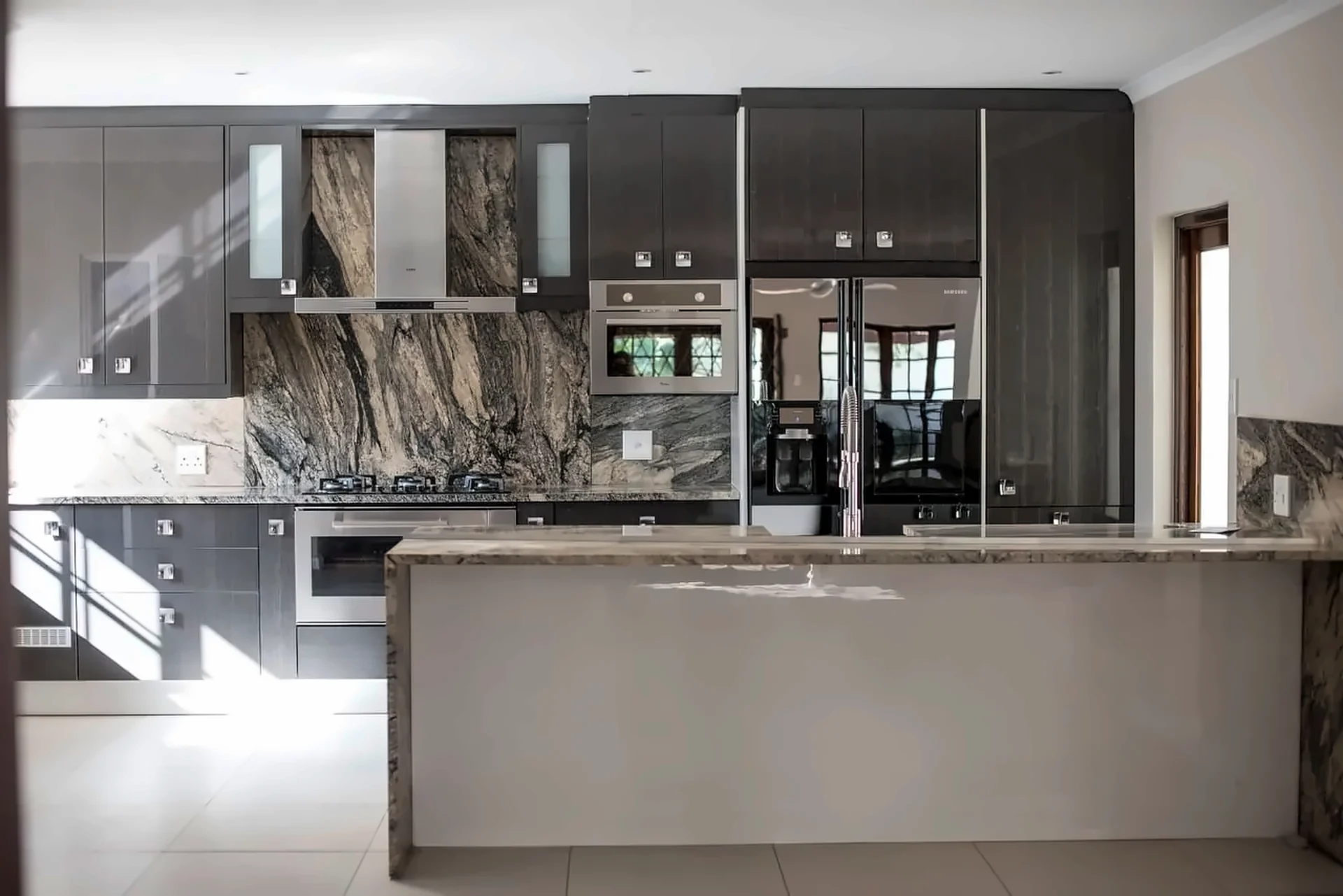 Dark cabinetry with a veined stone splashback and waterfall island