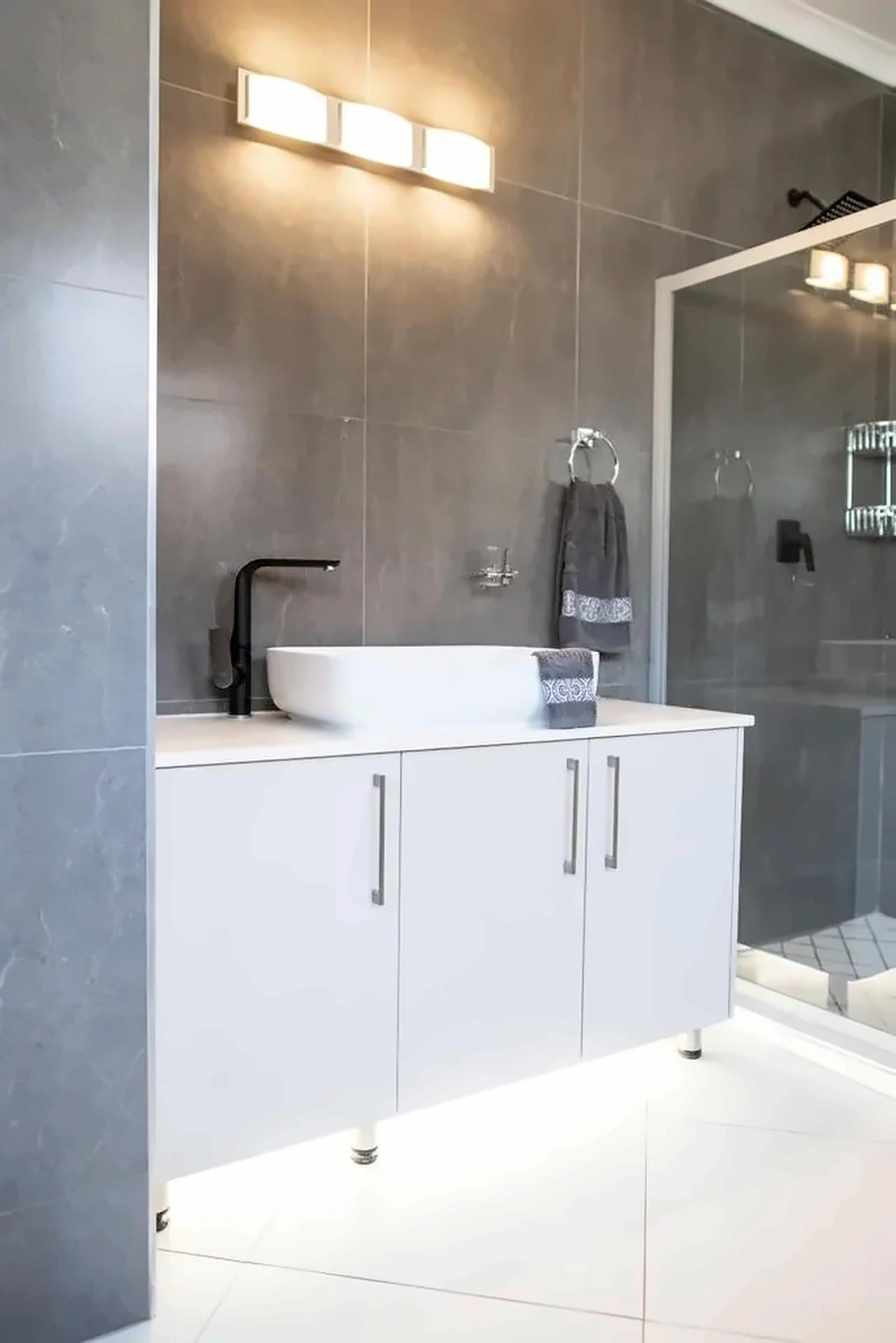 White vanity unit with under-lighting against grey tiling