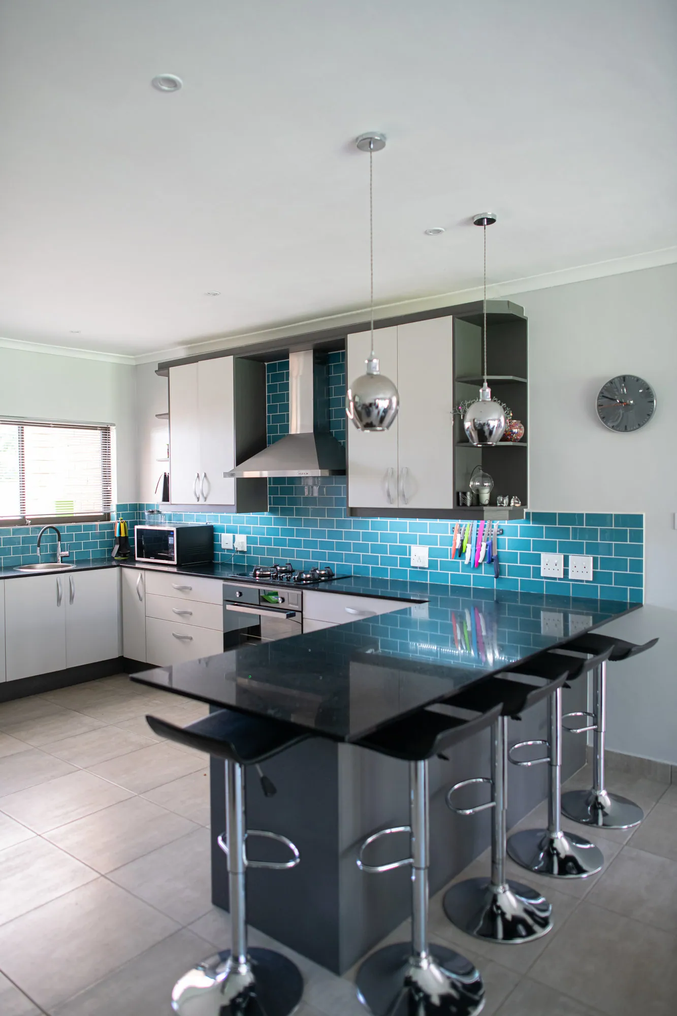 White kitchen with teal subway tiling, black worktops and a breakfast counter