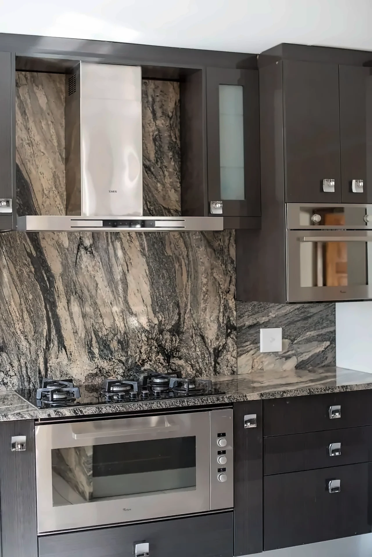 Dark cabinetry with marble-effect splashback, gas hob and built-in oven