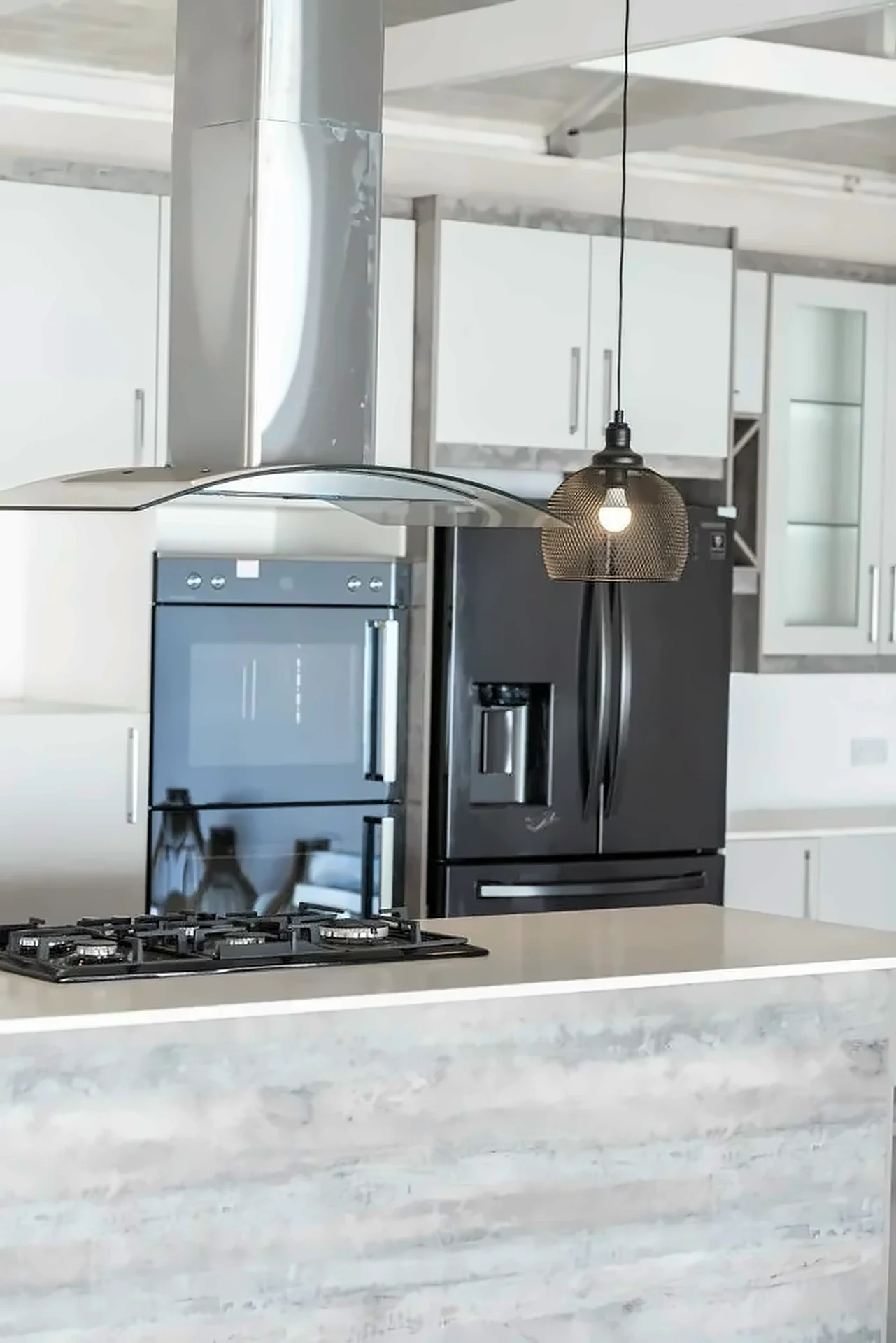 Double wall ovens and black fridge beside a stainless island extractor