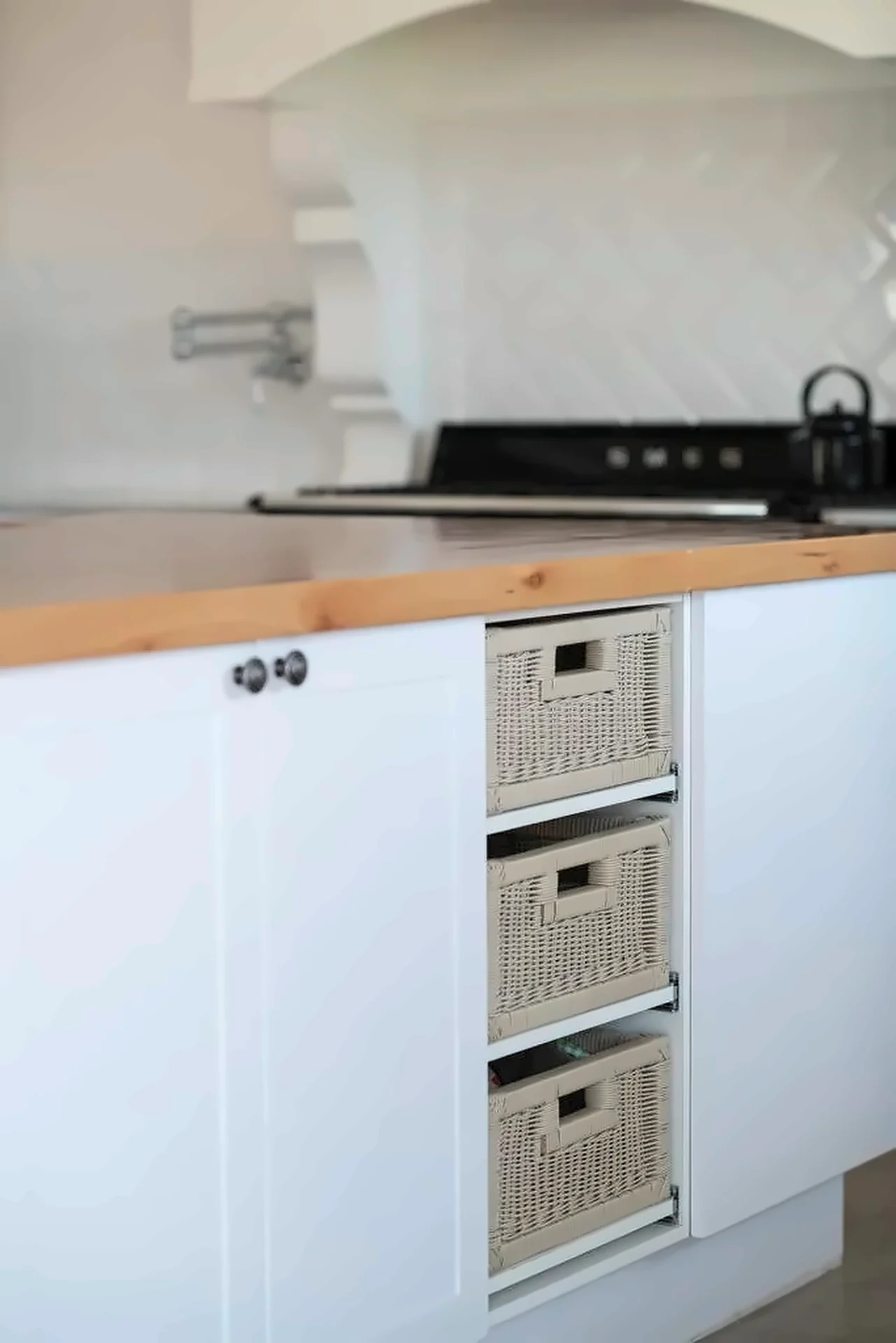 Butcher-block worktop above white cabinetry with woven baskets