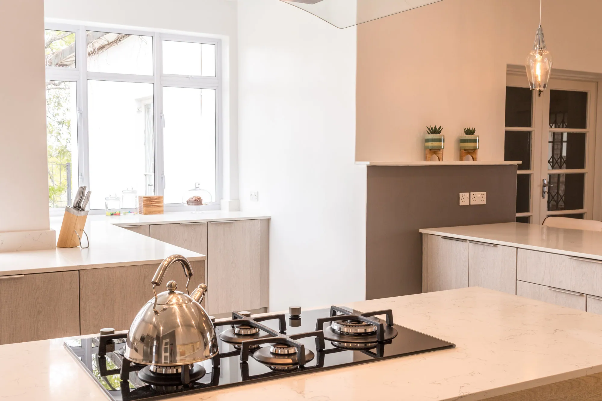 Gas hob set into a white stone worktop with a stainless kettle